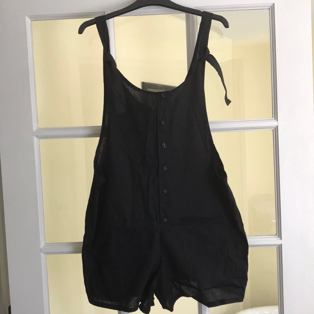 Black romper with pockets in front, button accents, and ties on shoulders.